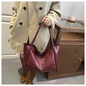 Macro shot of stylish burgundy tote bag with crocodile embossed leather texture