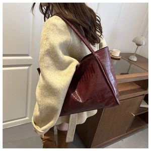 On-shoulder view of a large crocodile-embossed dark red tote bag on a wool coat