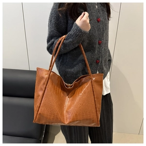 Close-up of a large caramel brown tote bag with crocodile texture and long shoulder straps