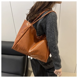 Close-up of caramel brown crocodile texture tote bag worn on shoulder in a cozy home setting