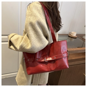 Detail of red leather tote bag with decorative metal buckle strap in indoor lifestyle setting