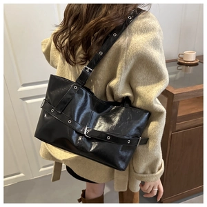 Detail of black glossy tote bag with adjustable buckle straps and metal eyelet accents