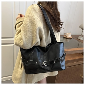 Detailed view of black patent leather tote bag with silver buckle worn on the shoulder