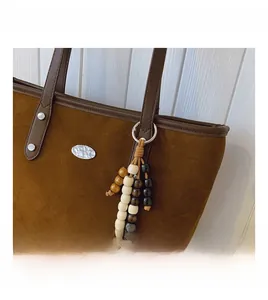 Détail du sac cabas en daim marron avec pompon en perles de bois et pièces argentées