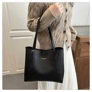 Detail of black leather tote bag with gold lettering shown on shoulder with beige sweater