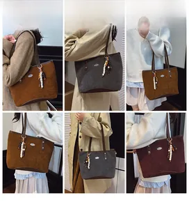 Détail du sac cabas en daim montrant le logo métallique et le pendentif pompon chic