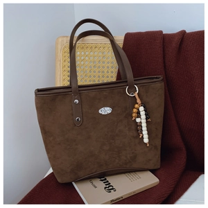 Détail d'un sac cabas en daim marron foncé avec plaque argentée et accessoire perlé