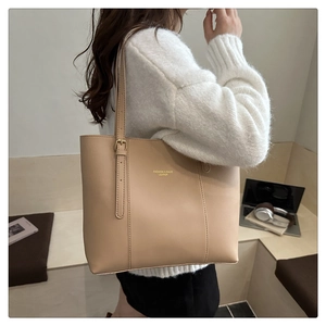Detail view of cream tote bag with gold logo and adjustable metallic strap buckle