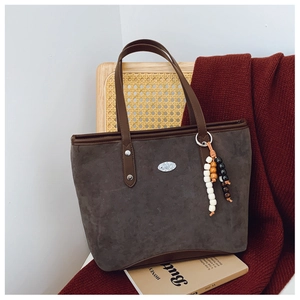 Détail du cabas en daim gris avec lanières en cuir marron et pendentif en perles