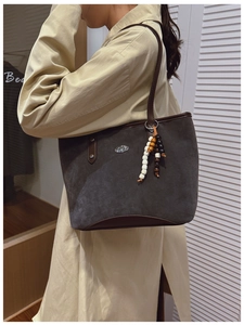 Détail d'un sac cabas en daim gris avec finitions en cuir marron et pendentif perlé