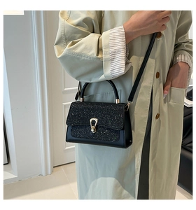 Detail of black tweed crossbody bag with golden buckle and sequined flap on a model