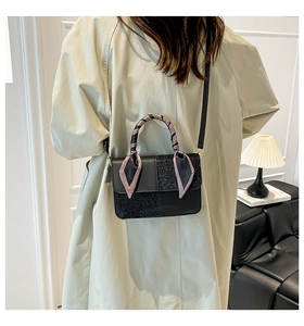 Detail of black crossbody bag with glitter panels and scarf-wrapped handle on a trench coat