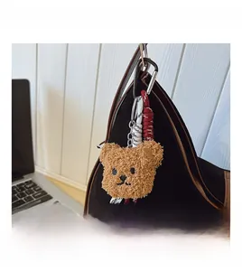 Close-up of a brown plush bear charm with woven lanyard on a black tote bag side