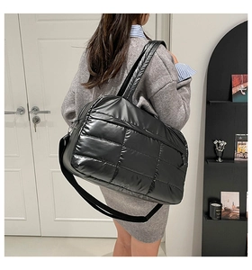 Detail of a large black quilted tote bag showing its high-gloss nylon texture and strap