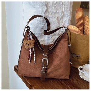 Detail of brown suede hobo bag with leather strap and a cute teddy bear charm