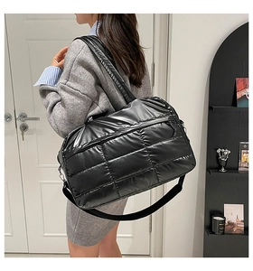 Detail of a large black quilted travel tote bag worn across the body by a female model