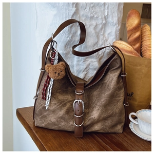 Detail of dark brown vintage tote bag with metal buckle and cute plush bear charm