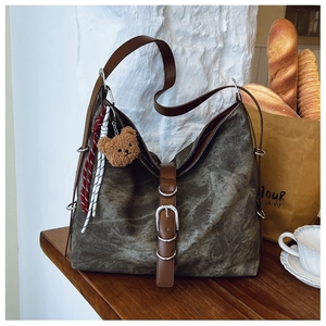 Detail of vintage green tote bag with brown leather straps and teddy bear ornament