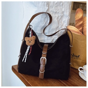 Close-up of black tote bag with silver buckle, brown strap and plush bear charm decoration