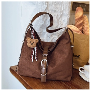 Detail of dark brown suede tote bag with leather strap buckle and plush bear charm