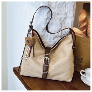 Detail of a large khaki suede tote bag with brown straps and a cute plush bear charm