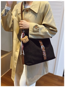 Black suede tote bag with brown leather trim and cute bear charm worn on a trench coat