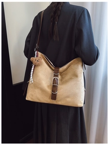 Detail view of khaki suede tote bag with brown leather accents and plush bear charm