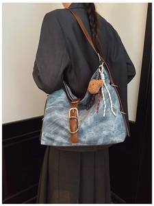 Detail of light blue vintage canvas tote bag with brown leather straps and plush bear charm