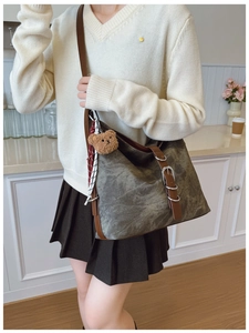 Detail of grey canvas tote bag with brown leather straps and plush bear charm