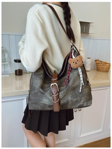 Detail of vintage gray canvas tote with leather straps and teddy bear charm on model