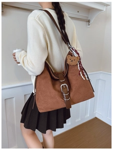 Detail of brown suede tote bag featuring silver round metal buckle and plush bear charm