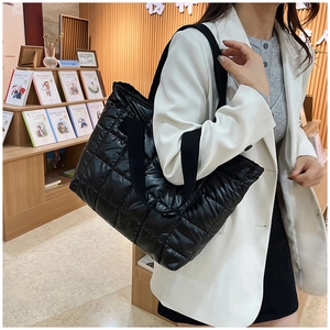 Détail du grand sac cabas noir matelassé avec finition brillante porté par un mannequin