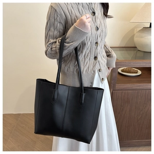 Close-up of a large black leather tote bag worn by a model in a cozy interior setting