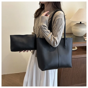 Detail view of black faux leather tote bag and pouch set on a model in beige sweater