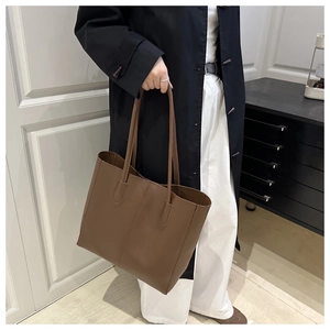 Détail d'un grand sac cabas en cuir marron avec coutures verticales porté par un mannequin