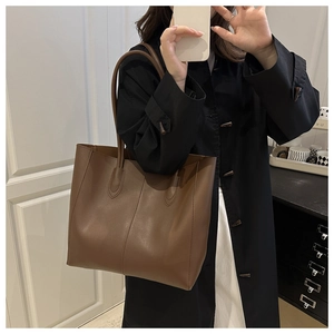 Close-up of a large brown leather tote bag with vertical stitching on a model