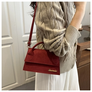 Detail of burgundy suede flap bag with gold logo on a knit sweater background