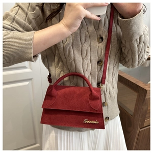Detail shot of red suede crossbody bag featuring a gold logo and top handle