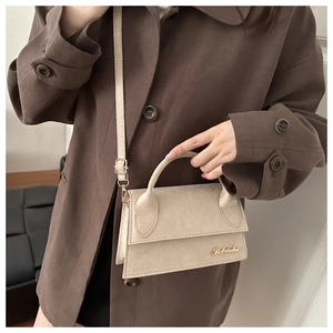 Detail of a beige suede small square bag with golden logo and adjustable strap
