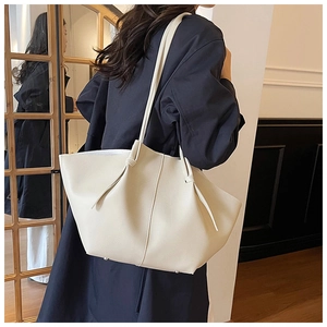 Close-up of cream leather tote bag with pebbled texture and metal feet on a model
