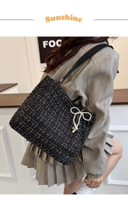 Detail einer schwarzen Tweed-Tasche mit Goldfaden, Perlenanhänger und Lederriemen