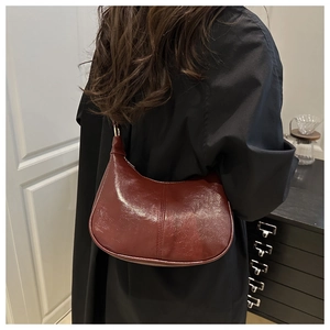 Close-up of burgundy glossy leather hobo bag worn by a model in a modern interior