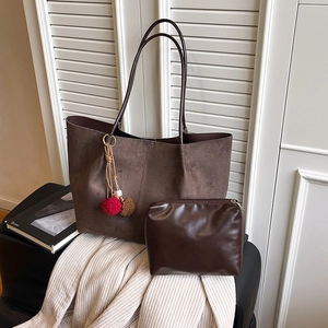 Brown suede tote bag with fur ball charm and matching pouch on a cozy knit blanket