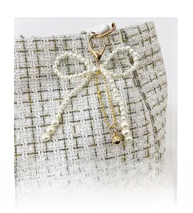 Detail eines Perlen-Schleifen-Anhängers mit Goldketten auf weißem Tweed-Taschengewebe