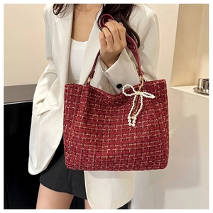Detail der roten Tweed-Handtasche mit Goldschimmer und Perlen-Schleifen-Anhänger an der Schulter