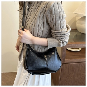 Close-up of black glossy leather half-moon bag with elegant stitching and gold hardware detail