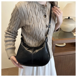 Detail of glossy black hobo shoulder bag with central stitching on a beige knit cardigan