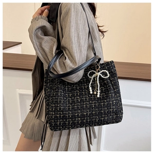 Seitenansicht der schwarzen Tweed-Tasche mit Perlenbogen-Anhänger an einem Modell