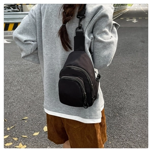 Detail of a black nylon crossbody bag featuring multi-zipper pockets and carabiner hook