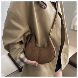 Brown suede crescent hobo bag shown worn over a khaki trench coat for an autumn style